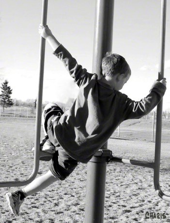 boy playing monkey bars bw